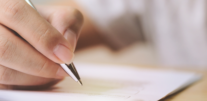 hand holding pen over piece of paper on table