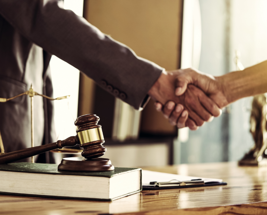 two hands shaking above desk with legal objects